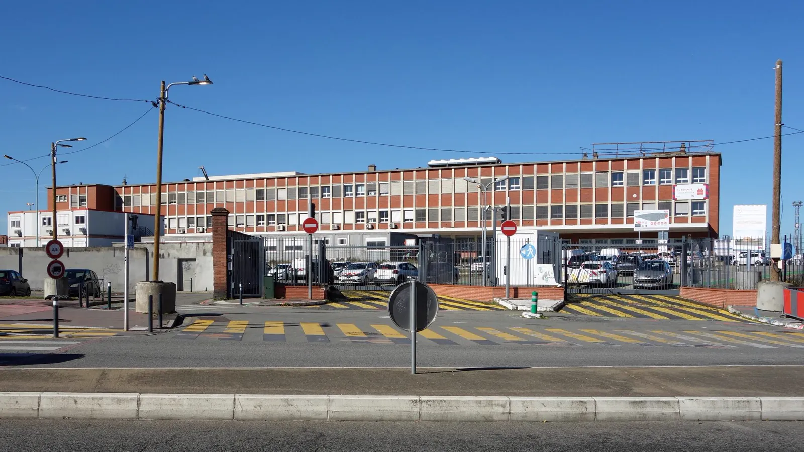 Immeuble de bureaux en briques à bandeaux de fenêtres, derrière un parking, sous un ciel bleu, avenue de Lyon à Toulouse