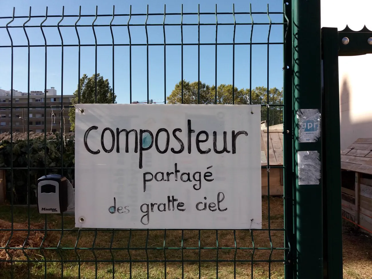 Affiche manuscrite « composteur partagé des gratte ciel » accrochée à une grille, rue Jean-Bourgey à Villeurbanne