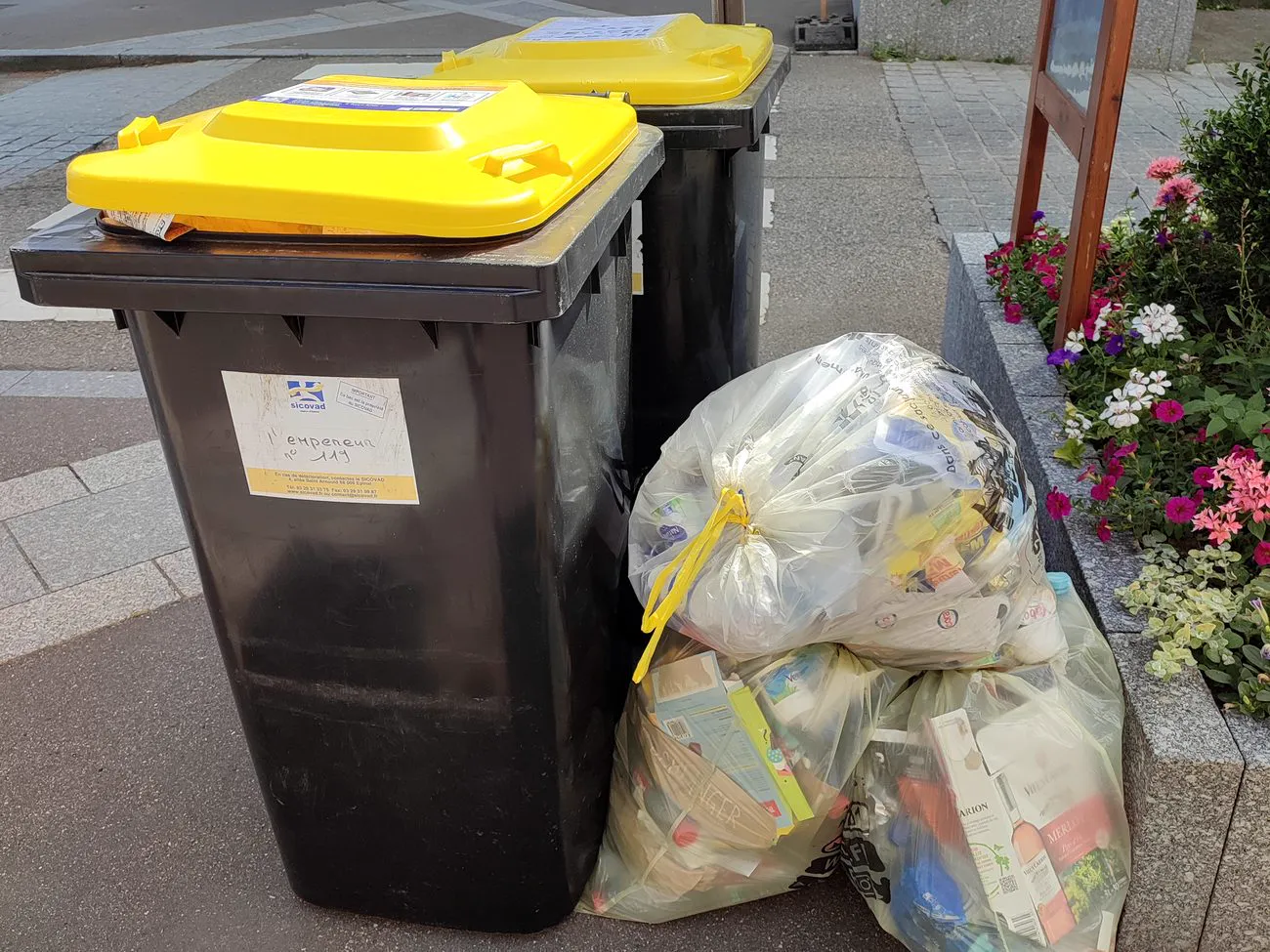 Deux bacs à couvercle jaune et des sacs jaunes d'emballages posés sur un trottoir, rue Charles-de-Gaulle à Remiremont